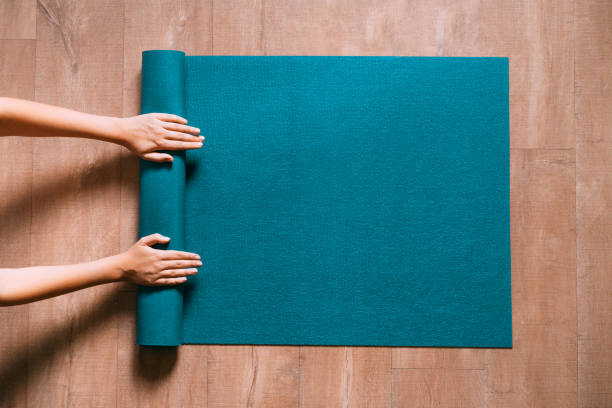 Femme déroulant un tapis de Yoga bleu sur sol en bois